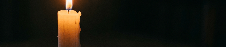 Lit candle in a holder on a wooden table casting warm light