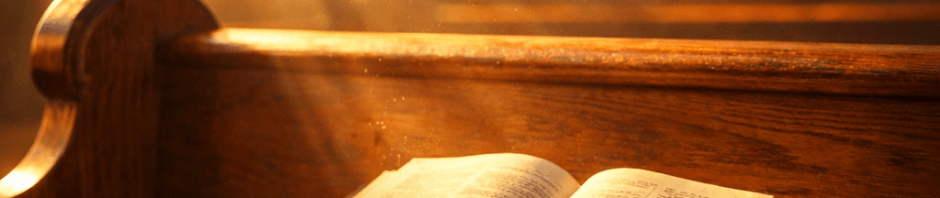 Open Bible resting on a wooden church pew under sunlight