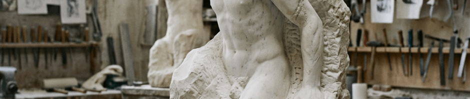 Marble sculpture of a male figure emerging from rough stone in a workshop with tools and drawings