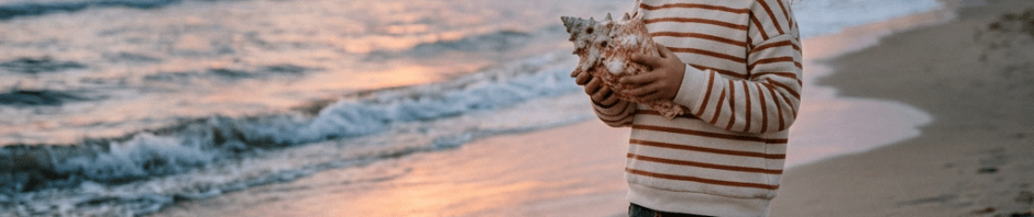 Child holding large seashell on beach at sunset
