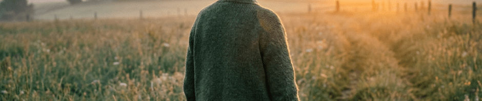 Elderly woman standing on a grassy path looking at the sunrise over fields
