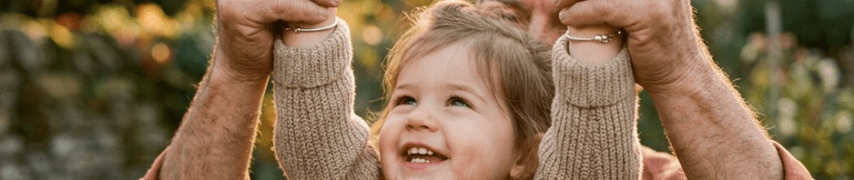 Adult holding up happy child's hands outdoors with autumn foliage