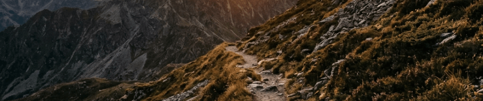 Mountain hiking trail with rocky terrain and sunset over distant peaks