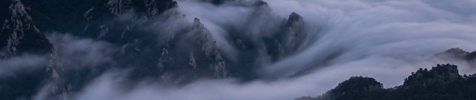 Hiker standing on rocky trail overlooking mist-covered mountains at dawn