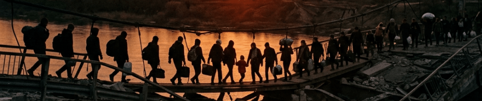 People carrying bags walking across a damaged bridge over a river at sunset