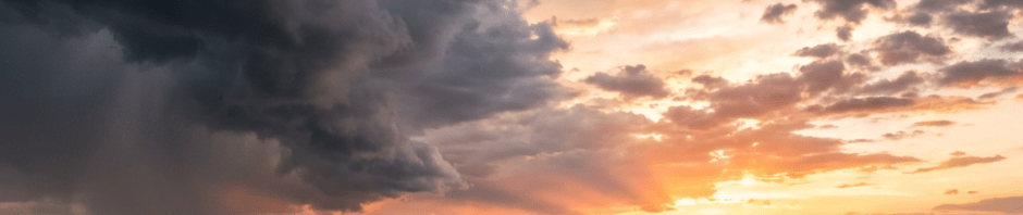 Sunset over mountains with dark storm clouds and rain on one side