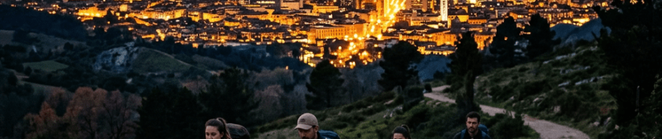 Four hikers walking on a rocky mountain path with a city illuminated at sunset behind them