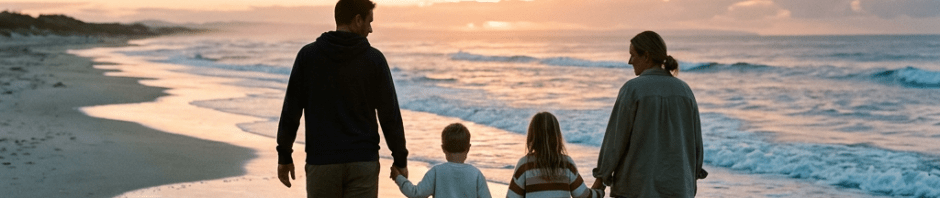 Family of four holding hands walking barefoot on beach at sunset